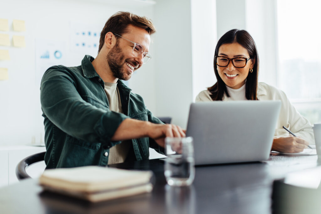 Two business people using a laptop together while sitting in a meeting. Happy business people looking at a slide presentation in an office